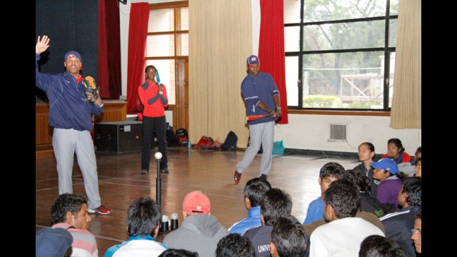 Natasha Watley, Barry Larkin, and Joe Logan teach batting skills indoors while highlighting the differences between batting in baseball and softball. 