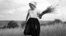 Photo of a woman standing in a field with hay in her hands.