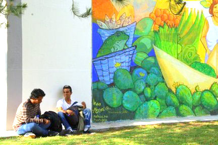 Two men sit outside against building with colorful art on it