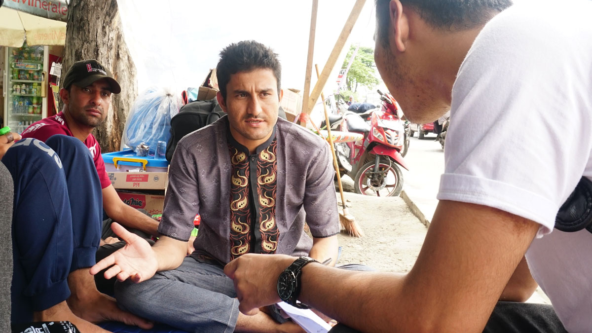 Man sitting with legs crossed and hands out looking puzzled at another man