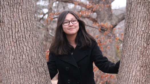 Young girl with dark hair and glasses posing between two tree trunks