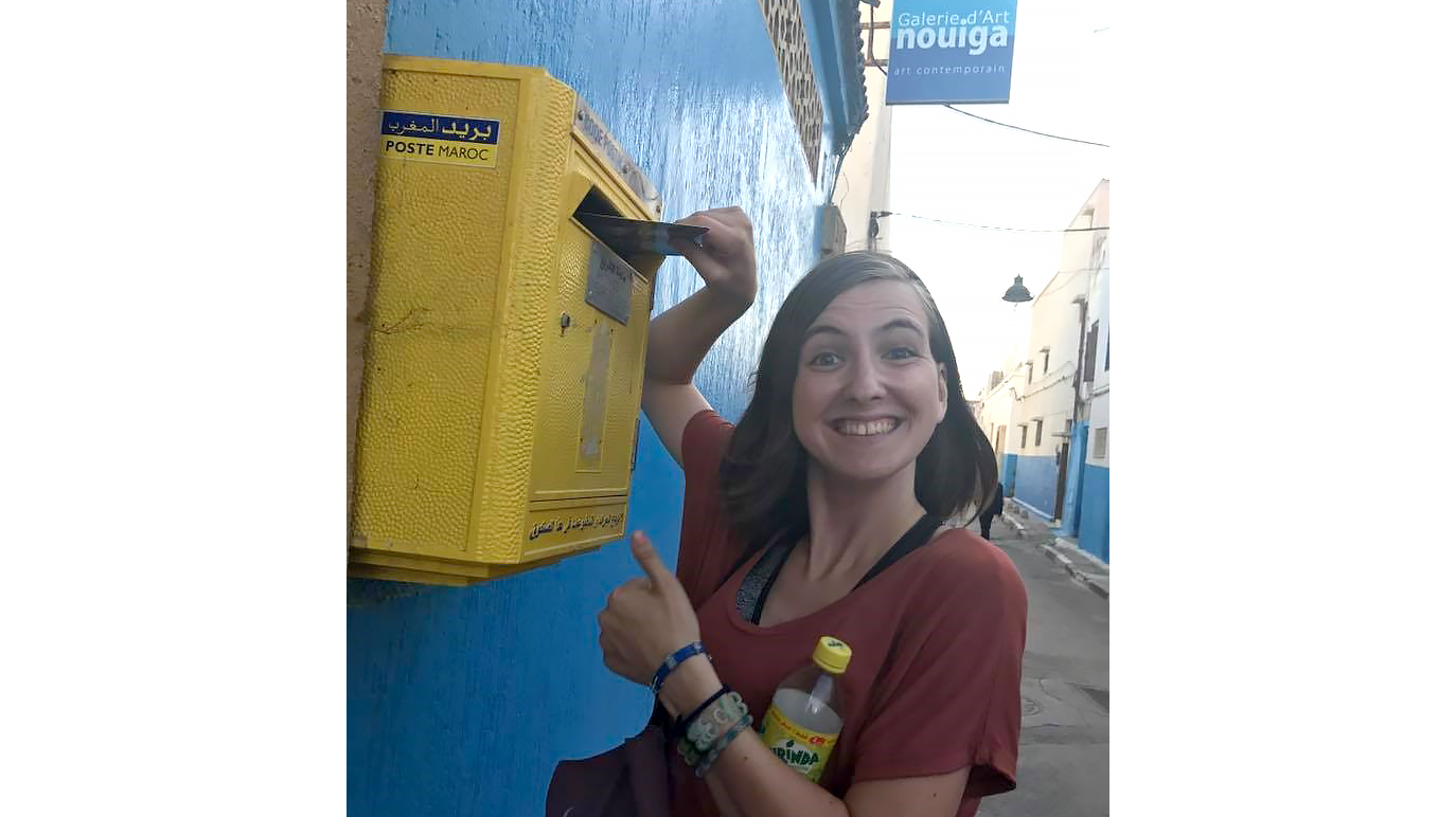 Woman placing mail in a mailbox while looking at the camera smiling with a thumb up