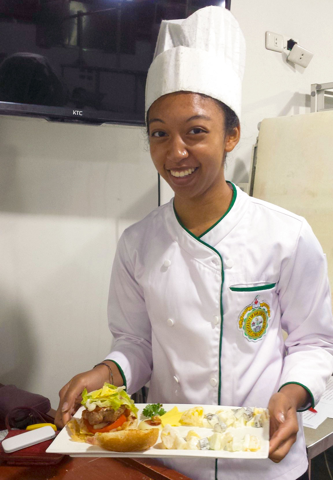 Young woman in chef attire holding plate of food