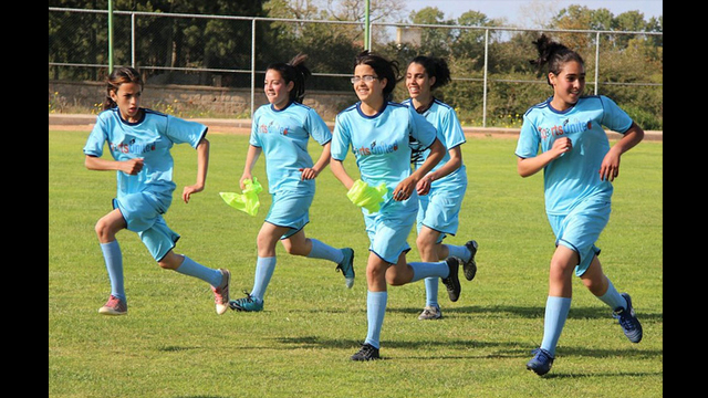 A group of teenage girls run together during a soccer clinic in Morocco.