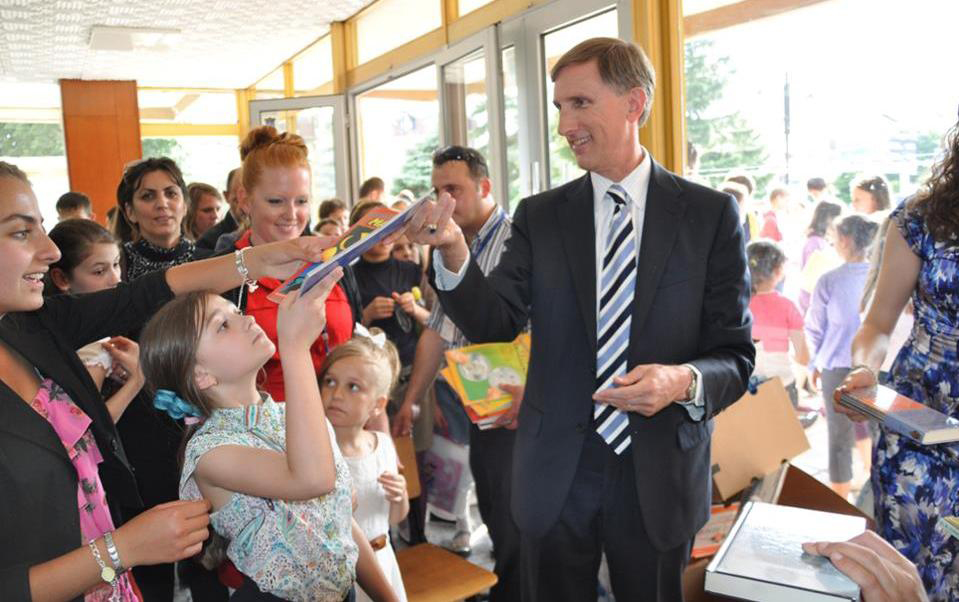 Fulbright English Teaching Assistant Jennifer Birdsall (in red) with U.S. Ambassador to Macedonia Paul Wholers as he hands donated English children&#039;s books out to local children at the American Corner Tetovo.
