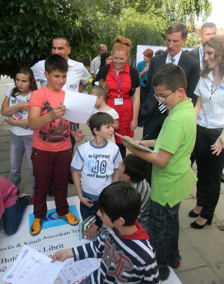 Fulbright English Teaching Assistant Jennifer Birdsall (in red) and U.S. Ambassador to Macedonia Paul Wholers watch at the American Corner in Tetovo as children collect books donated by communities in Nebraska.