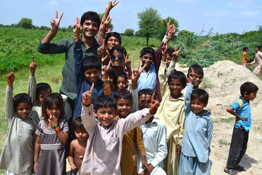 Young man stands with group of small kids all smiling and holding up two fingers