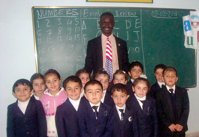 Man stands with group of small children in front of chalkboard