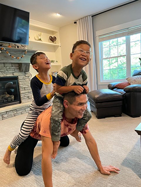 Image of Shon giving two laughing boys a piggy back ride in the living room.
