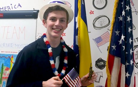 Young man in patirotic hat and lanai holding U.S. flag and miniature Statue-of-Liberty