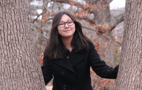 Young girl with dark hair and glasses posing between two tree trunks