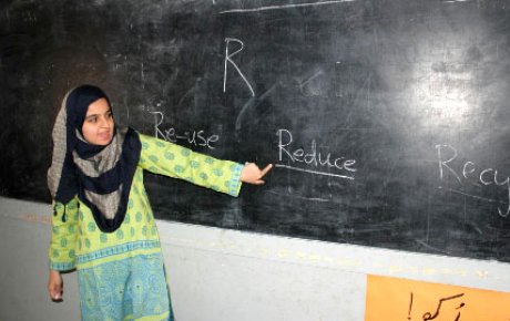 Young woman wear hijab pointing at a chalkboard with the letter R and the words Re-use, Reduce, and Recycle