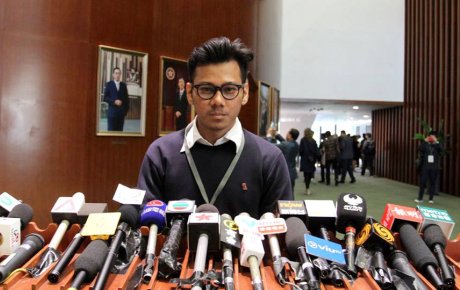Man stands at podium filled with media microphones
