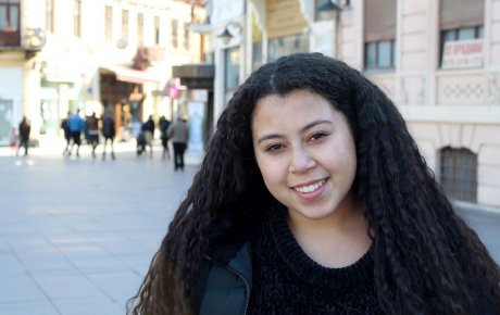 Young woman with long thick hair standing on a city street with people walking in the background