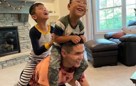 Image of Shon giving two laughing boys a piggyback ride in the living room.