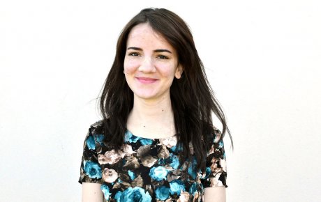 Young woman grinning wearing a flowery dress against a blank background