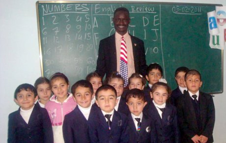 Man stands with group of small children in front of chalkboard