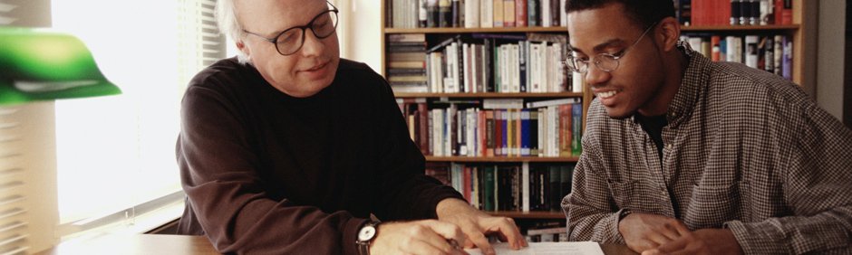 Image of a teacher and a student sitting at a table reviewing a book.