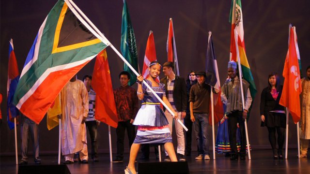Girl in festive attire walks across stage holding a large South African flag
