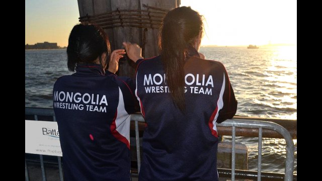 From a pier in New York Harbor, Mongolian wrestlers see the Statue of Liberty in the distance.