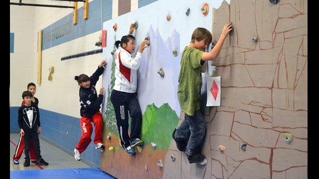 Mongolian wrestlers try out a climbing wall with students during their visit to an elementary school in Parker, CO.