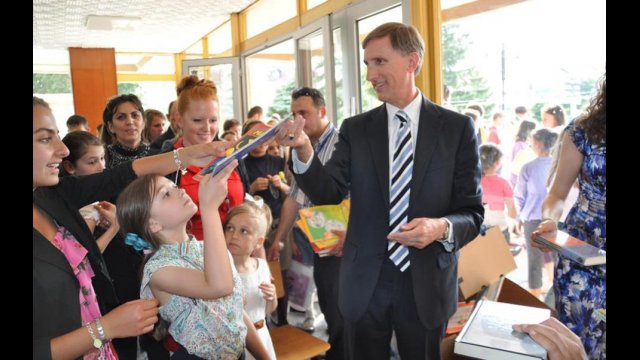 Fulbright English Teaching Assistant Jennifer Birdsall (in red) with U.S. Ambassador to Macedonia Paul Wholers as he hands donated English children&#039;s books out to local children at the American Corner Tetovo.