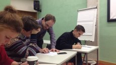 Three students at desks in a classroom with male teacher leaning over one desk