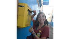 Woman placing mail in a mailbox while looking at the camera smiling with a thumb up