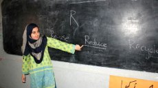 Young woman wear hijab pointing at a chalkboard with the letter R and the words Re-use, Reduce, and Recycle