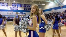 Teen girl in cheerleading outfit stands on court facing camera surrounding other cheerleaders