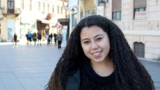 Young woman with long thick hair standing on a city street with people walking in the background