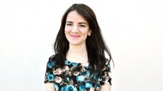 Young woman grinning wearing a flowery dress against a blank background