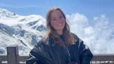 A photo of Julia posing near a fence, with a mountain backdrop behind her