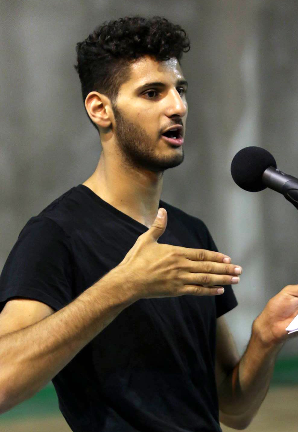 Young man stands in front of microphone talking