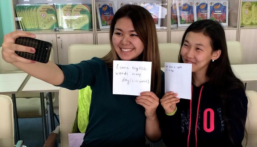 Girls taking a selfie with cell phone while holding up handwritten signs