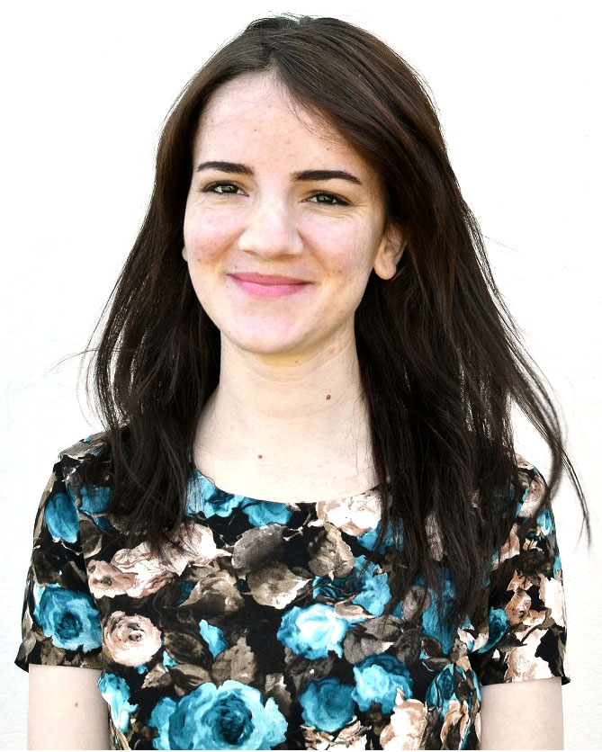 Young woman grinning wearing a flowery dress against a blank background